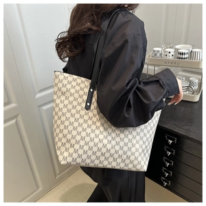 Detail of large tote bag with M-letter print and black leather straps worn by a model