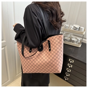 Close-up of the orange-pink tote bag featuring repeating brown M prints and black straps