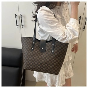 Detail of large brown tote bag with M monogram pattern and black leather handles