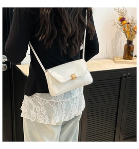 Close-up of a white patent leather baguette bag with a golden square lock on a model