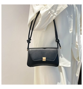 Close-up of minimalist black baguette bag with gold buckle and knotted strap detail