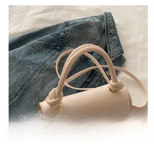 Detail of cream square bag with crocodile embossing, knotted handle, and gold hardware