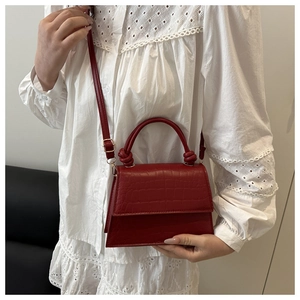 Red crocodile embossed handbag with knot handle detail and adjustable leather crossbody strap