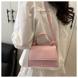 Detail of pink croc-effect handbag featuring a knotted handle on white lace dress