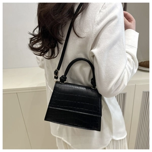 Detail view of the black crocodile pattern texture and knotted handle on the leather handbag
