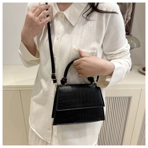 Detail shot of a black crocodile-embossed handbag featuring a gold buckle and knot handle