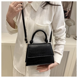 Detail of black crocodile texture handbag held by model in cream shirt and indoor setting