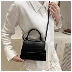 Close-up of black crocodile-embossed mini handbag with a knot detail top handle