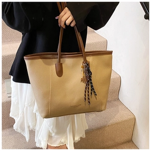 Close-up of khaki pebbled leather bucket bag with brown handles and woven tassel charm