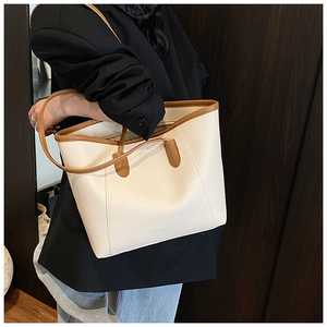 Detailed view of cream bucket bag with brown trim and litchi texture on a model
