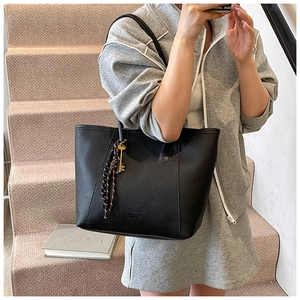 Detail of black lychee grain leather tote bag with gold charm and striped lanyard strap
