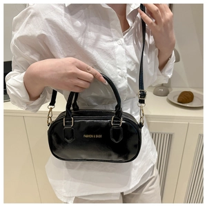 Detail of model wearing a black glossy pillow-shaped handbag with golden metal hardware