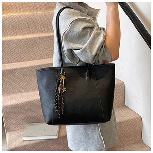 Detail of black lychee grain tote bag with gold key charm and striped woven strap decoration