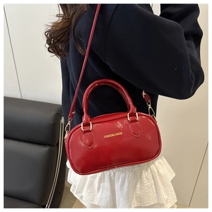 Borsa bowling rossa lucida con finiture dorate indossata a tracolla su abito casual