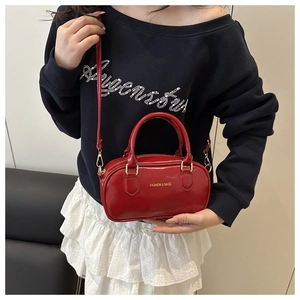 Détail du sac Boston rouge avec garnitures dorées et lettrage porté par un mannequin