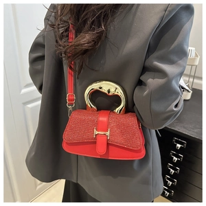 Detail of red crossbody bag with sequin texture and golden H-shaped clasp on a grey suit