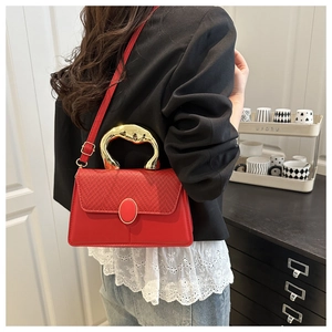 Macro detail of red crossbody bag with woven flap and irregular gold metal handle