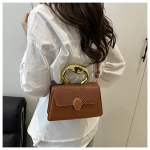 Detail of brown leather handbag with woven flap and artistic gold lava handle on model