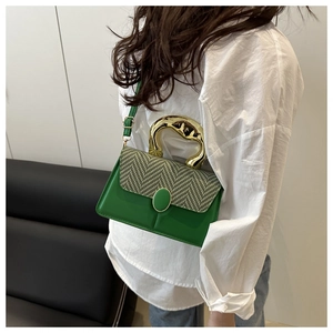 Detail of green leather handbag with herringbone fabric flap and golden sculptural handle