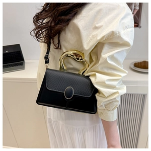 Detail of a black leather crossbody bag with a modern gold metal handle and flap closure