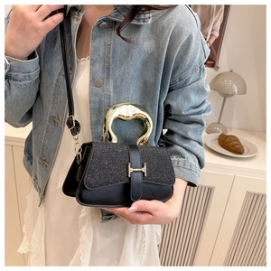 Detail einer eleganten schwarzen Handtasche mit goldenem H-Verschluss und Metallgriff