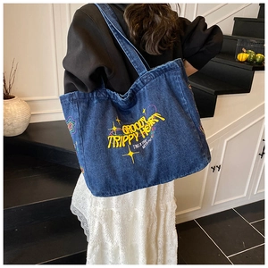 Detail of blue denim tote bag featuring retro GROOVY TRIPPY HEART embroidery on the front