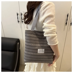 Photo lifestyle d'un sac cabas en toile rayée porté par un mannequin dans un salon moderne