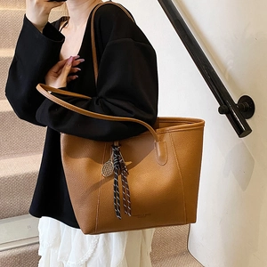 Brown litchi leather bucket bag with tennis racket charm and tassel on female model