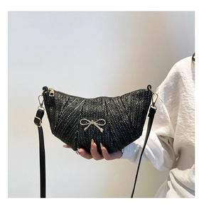 Detail view of woven crescent bag with gold bow ornament and adjustable leather strap
