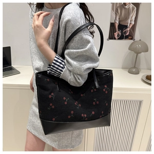Detail of canvas tote bag with cherry print and leather bottom on a model