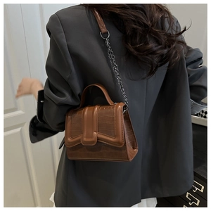 Brown crocodile leather handbag with silver chain worn over a grey blazer on person