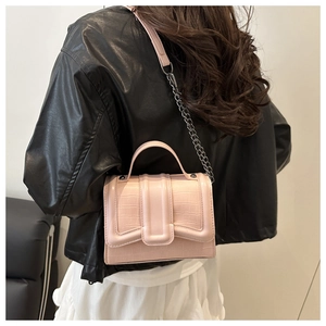 Pink faux crocodile leather bag detail showing the metal chain strap on a black jacket