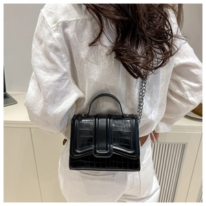 Detail of small black crocodile pattern bag with chain strap worn by a model