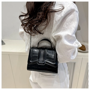 Detail of black crocodile texture leather bag with chain strap held by model