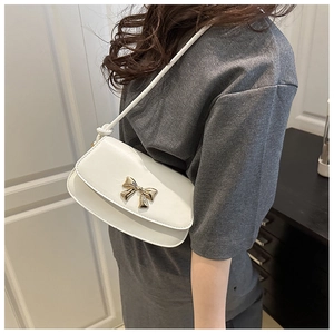Détail d'un sac à bandoulière blanc avec un nœud doré et une bandoulière à nœuds
