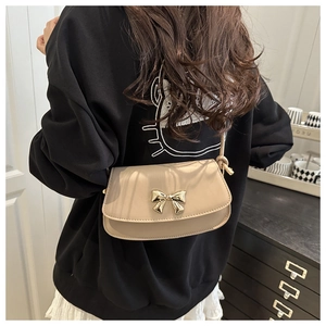 Detail of a creamy beige crossbody bag featuring a golden metal bow and matte leather finish