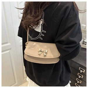Beige crossbody bag with gold bow buckle worn by model in a stylish indoor setting