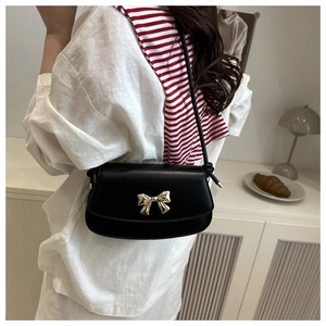 Gros plan d'un sac bandoulière en cuir noir avec fermoir noeud doré sur un mannequin