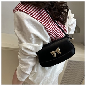 Détail d'un sac bandoulière en cuir noir avec nœud doré sur une tenue blanche décontractée