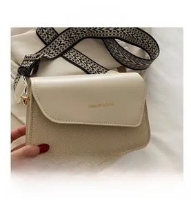 Detail of cream flap bag with woven texture and wide geometric pattern shoulder strap