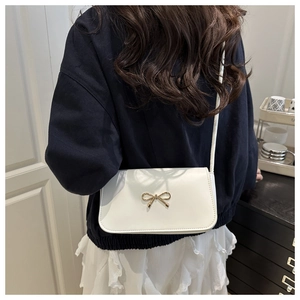 Detail of white leather shoulder bag featuring a gold bow clasp and sleek rectangular flap