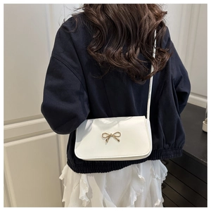 Detail view of a white rectangular crossbody bag with a gold metal bow on a model