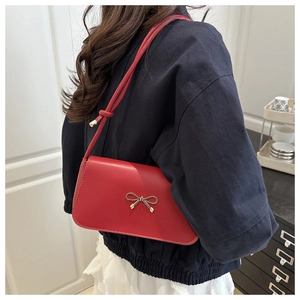 Detail of red leather shoulder bag with a gold bow accent and slim strap on a model