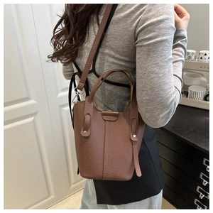 Macro detail of brown lychee-pattern leather bucket bag with silver metal buckles and straps