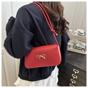 Detail of red small square bag with golden bow clasp and thin strap worn over shoulder