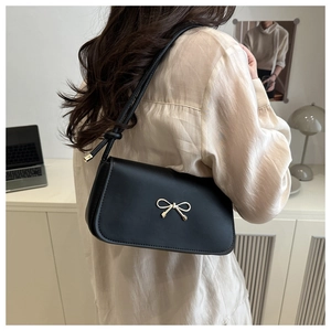 Dettaglio borsa sottobraccio in pelle nera con fiocco dorato e tracolla annodata elegante