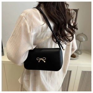 Detail of minimalist black PU leather shoulder bag featuring a golden bow metal hardware