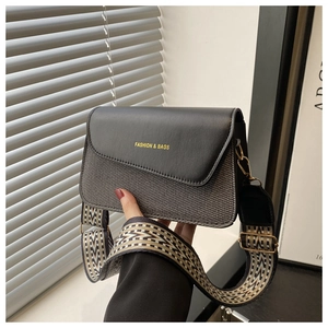 Detail of crossbody bag with black leather flap, gray woven texture and wide geometric strap
