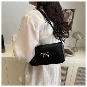 Detail view of a black baguette bag with gold bow clasp and stylish knotted shoulder strap
