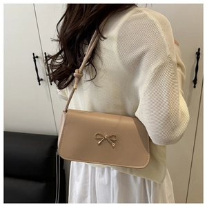 Detail of light beige shoulder bag with golden metal bow buckle and knotted strap